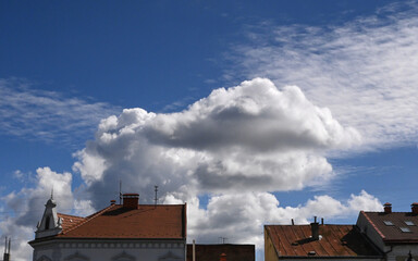 Beautiful cloud formations over rooftops under a bright blue sky in the afternoon