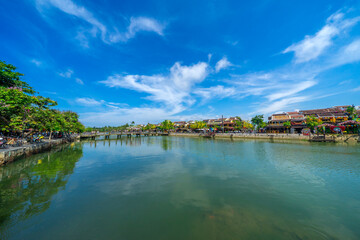 Fototapeta premium Wooden boats on the Thu Bon river in Hoi An ancient town. Yellow old houses on waterfront reflected in river. Hoi An is a UNESCO world heritage site in Vietnam