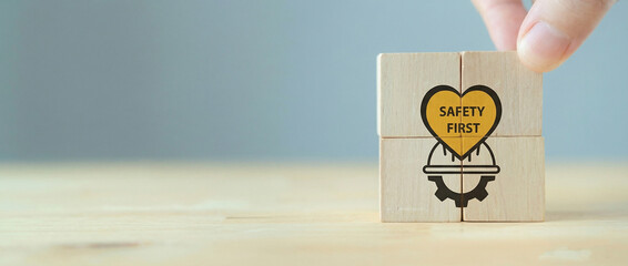Hand placing a wooden block labeled "SAFETY FIRST" inside a heart, completing the puzzle representing occupational health, hazard prevention, and essential workplace safety protocols