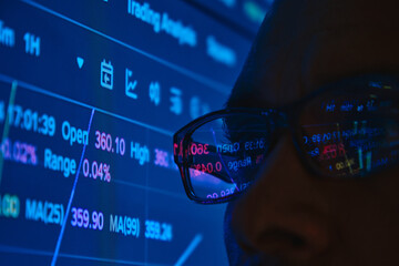 Person focusing on financial charts and cryptocurrency trading data on a blue screen