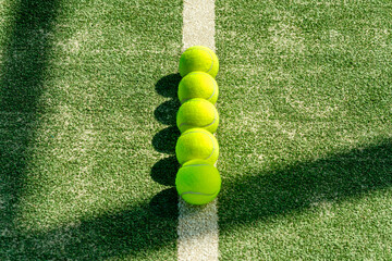 Row of bright yellow tennis balls lined up on a sunlit court. Clean composition with selective focus, showcasing sportlife, training atmosphere, and active lifestyle detail.