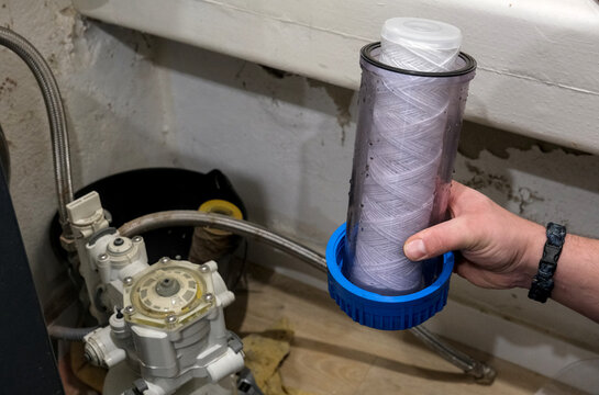 A person holds a cartridge filter near a water softener system, showing maintenance in a utility area.