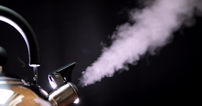 Water is boiling in a kettle and steam is coming out of the spout. Steam on a black background.