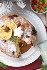 Tasty Christmas panettone cake with powdered sugar and festive decor on white table, flat lay