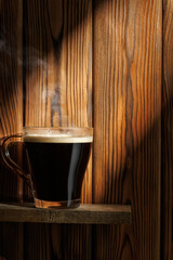 Ray of light falls on transparent cup of coffee standing on board against wooden background