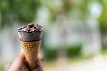 Chocolate ice cream in hand against nature background
