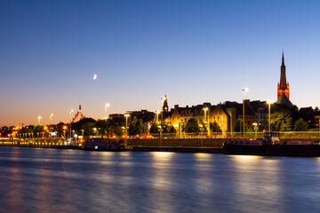 Fototapeta premium Evening City Landscape With Moon And Lights Reflecting In The River