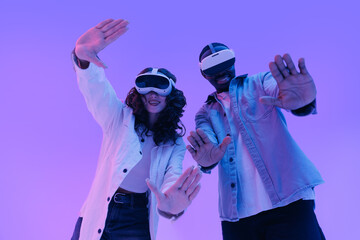 Fashion Immersive and futuristic innovation technology with AI concept. Young Asian woman and American African male experiencing virtual reality with headsets in neon lighting
