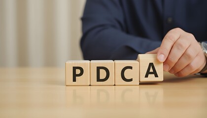 Hand placing wooden block to complete PDCA acronym on table.