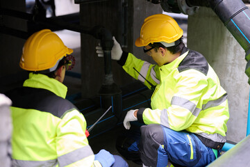 Fototapeta premium Two construction workers wearing safety vests and hard hats are focused on their work in factory