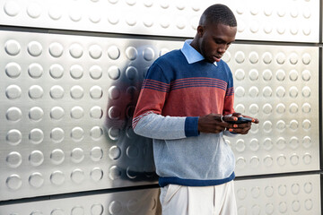 Fashionable man engaged with smartphone against modern metallic backdrop in urban setting