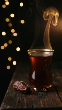Traditional glass of tea with rising steam and dried date on wooden table with warm bokeh lights for ramadan iftar or cozy evening authentic local flavor concept