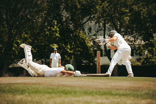 Cricket match action showing diving attempt and wicketkeeping scene