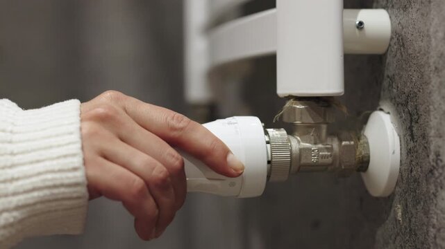 A hand adjusts the radiator temperature, highlighting energy saving, heating, and home comfort. Concept energy-efficient living and winter home solutions