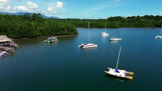 Aerial drone dolly approach to moored catamaran, sailboat, outrigger boat and a bamboo harbor in Tambobo Bay. Siaton, Negros Oriental, Philippines
