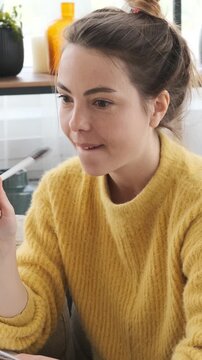 Cheerful young woman thinking and writing a to-do list or plans in a paper notebook, smiling and looking inspired while sitting on sofa at home. Vertical video.