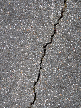Nahaufnahme eines diagonalen Risses in schwarzem Asphalt