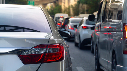 Rear side of luxury grey car driving on the road. Traffic jam on the road with many car at day time. Blurred of many car with town.