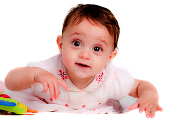 A baby girl is lying on her stomach, looking at the camera with a smile.