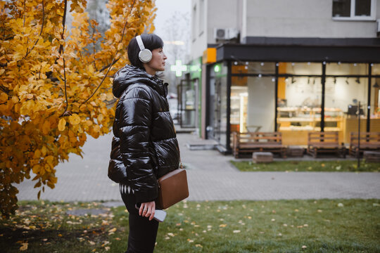 Urban wellness concept: woman having therapeutic walk with headphones, combining movement, music, and nature for mood boost, Copy space