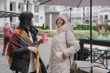 Happy multigenerational female friends enjoy outdoor meetup, checking smartphones and capturing memories with playful selfie on cold day