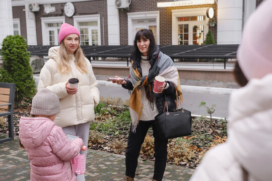 Happy multigenerational female friends enjoy outdoor meetup, checking smartphones and capturing memories with playful selfie on cold day