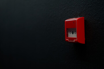 Side view of a red manual fire alarm call point mounted on a modern textured black wall. Emergency safety button behind glass with copy space. Photo