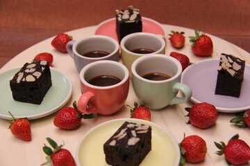 Top view of four pastel espresso cups filled with coffee, paired with brownies and fresh strawberries on matching plates. A cozy inviting dessert and coffee setup perfect for cafés lifestyle visuals