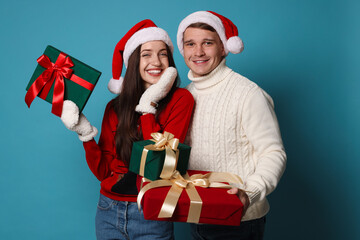 Happy couple in Santa hats with Christmas gifts on light blue background
