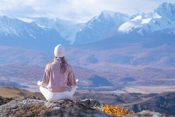 A woman sits in a meditative pose on a rocky outcrop, practicing yoga in the fresh mountain air. Surrounded by autumn colors, she enjoys the serene landscape and tranquility copy space