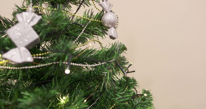 Woman hand decorating green Christmas tree with silver baubles, gold beads chain, festive holiday tree and toys. Christmas tree decorations. Decorating Christmas tree. New Year spirit.