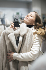 Obraz premium In a chic fashion boutique, a young woman savors the moment as she clutches a luxurious white fur coat, imagining it as her ideal New Year's gift during festive shopping.