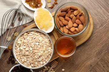 Making granola. Oat flakes in bowl, dried fruits, almond nuts and honey on wooden table, flat lay