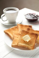 Fresh toasted bread slices served with butter, jam and tea on white wooden table