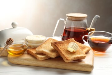Fresh toasted bread slices served with butter, honey and tea on white wooden table