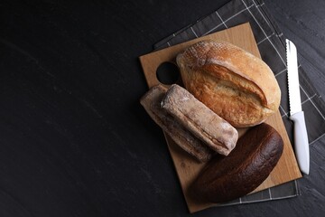 Different types of bread loaves and knife on black table, flat lay. Space for text