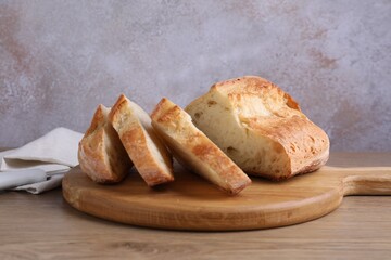 Cut fresh bread and knife on wooden table, closeup