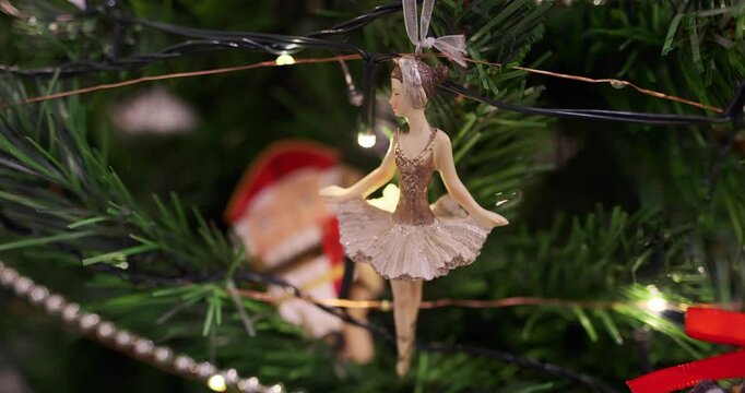 Ornament ballerina on Christmas tree branch with warm fairy lights and silver beads, wooden nutcracker figure in background, festive holiday decoration, closeup macro view. Christmas tree decorations