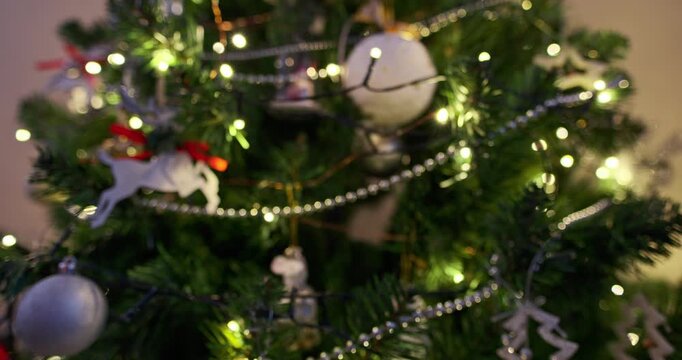 Defocused Christmas tree with glowing warm fairy lights, silver baubles, wooden reindeer and bead garlands creating soft bokeh circles, cozy festive winter holiday background