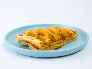 Golden flaky puff pastry with lattice pattern on a blue plate, isolated on a clean white background