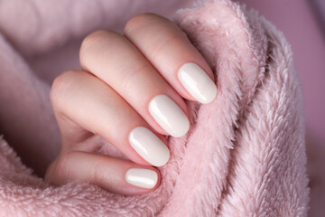 Female hand with beautiful manicure - cloud white dancer nails on pale pink fluffy fabric, textile...