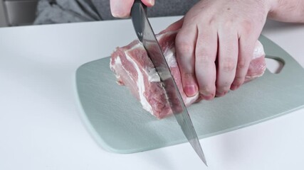 Person's hand slicing fresh raw pork loin with a sharp kitchen knife on a grey cutting board, showcasing domestic culinary skills for healthy meal preparation