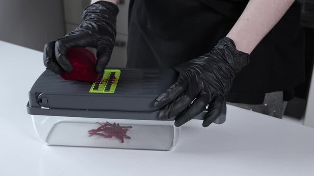 A person wearing black protective gloves carefully grates a vibrant red beetroot using a modern mandoline slicer, emphasizing safe and efficient vegetable preparation for healthy cooking