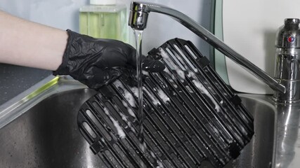 Person in black glove washing a removable air fryer grill rack with soap and water in a kitchen sink, emphasizing kitchen hygiene and appliance maintenance