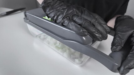Person in black gloves utilizing a versatile grey and green vegetable chopper to precisely dice an onion, enhancing kitchen productivity for quick meal preparation