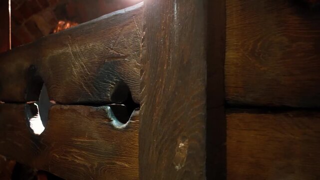 Dark medieval pillory punishment stocks made of old, weathered wood illuminated by a flickering light source, creating a dramatic and historical atmosphere inside a dungeon or ancient castle