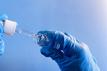Dropping liquid from a pipette into a glass vial while wearing blue gloves in a laboratory setting