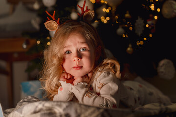Portrait of a Caucasian child little girl in the dark by a Christmas tree with a garland, her face beautifully illuminated