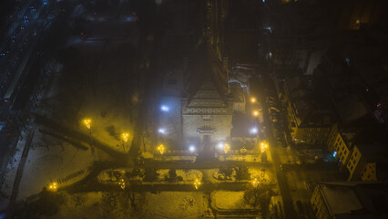 Widok z drona na nocne Stare Miasto w Toruniu, spowite delikatną mgłą. Podświetlone budynki i zabytkowa architektura lśnią w mgiełce, tworząc tajemniczy i nastrojowy miejski pejzaż.