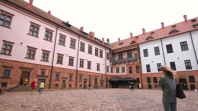 Tourists exploring the historic cobblestone courtyard of the mir castle complex, a unesco world heritage site in belarus, showcasing medieval gothic and renaissance architecture